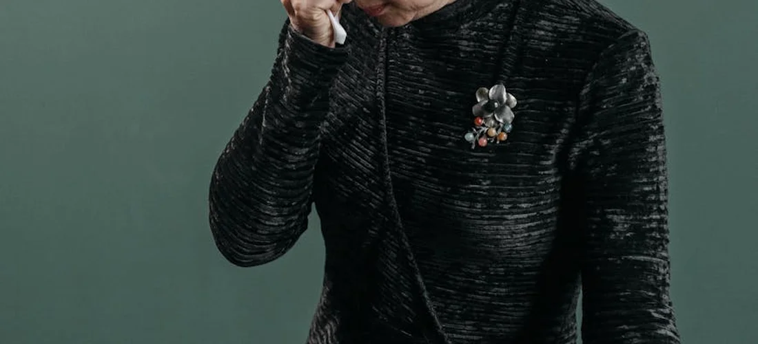 Close-up of a person in a dark, textured suit wearing a boutonniere against a muted green background.