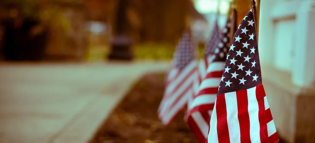 Row of American flags along a sidewalk with a blurred background