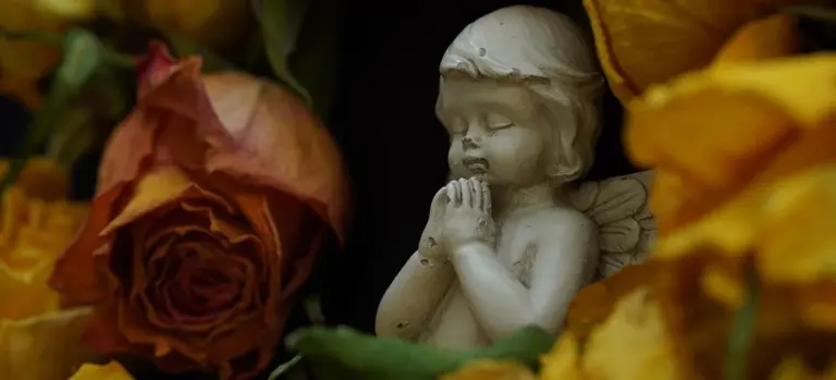 A small praying angel statue nestled among yellow and orange flowers.