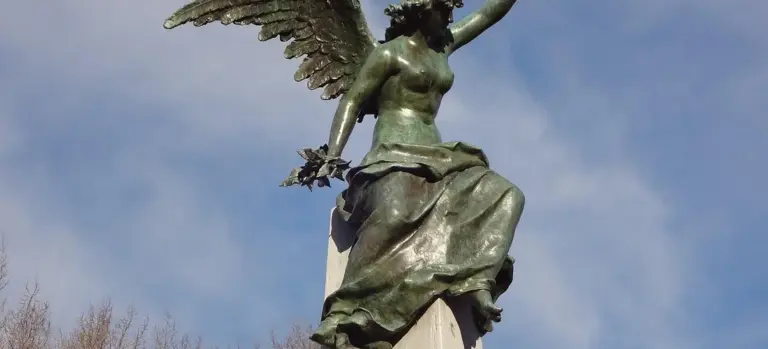 Bronze angel statue with outstretched wings perched on a pedestal against a clear blue sky