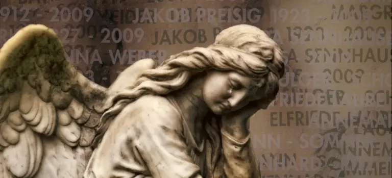 A marble angel statue with a bowed head and outstretched wings, set against a muted background of engraved names and dates.