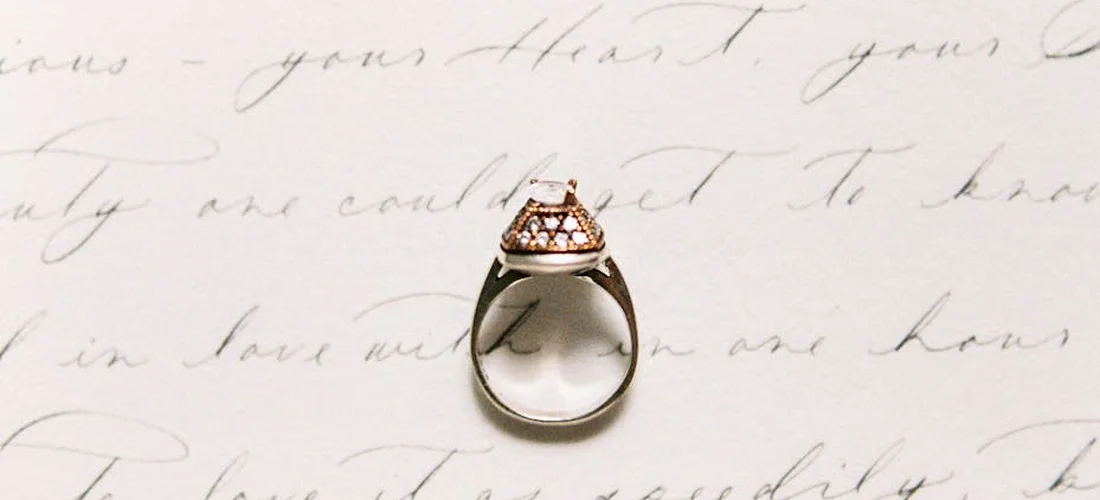 Close-up of a ring with a clear memorial diamond centerpiece on a light background with cursive handwriting.