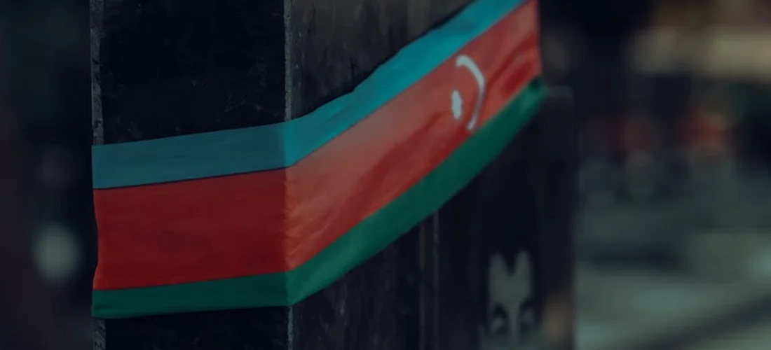 Close-up of a memorial or monument wrapped with a ribbon resembling the Azerbaijani flag (blue, red, and green stripes) with a white crescent.