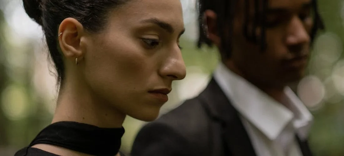 A somber woman in profile with a blurred man in the background, representing mourning and the emotional weight of bereavement leave.