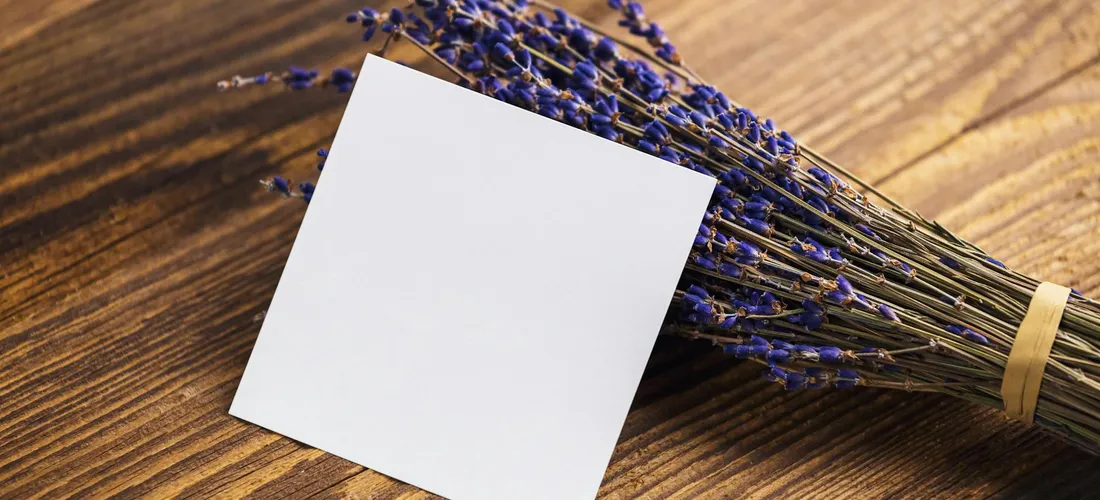 Blank square condolence card beside a bundle of lavender flowers on a wooden surface