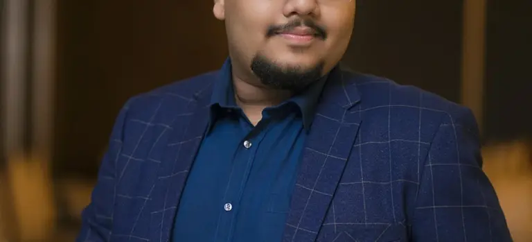 Portrait of a man wearing a blue blazer and matching blue shirt, posed in a neutral setting.