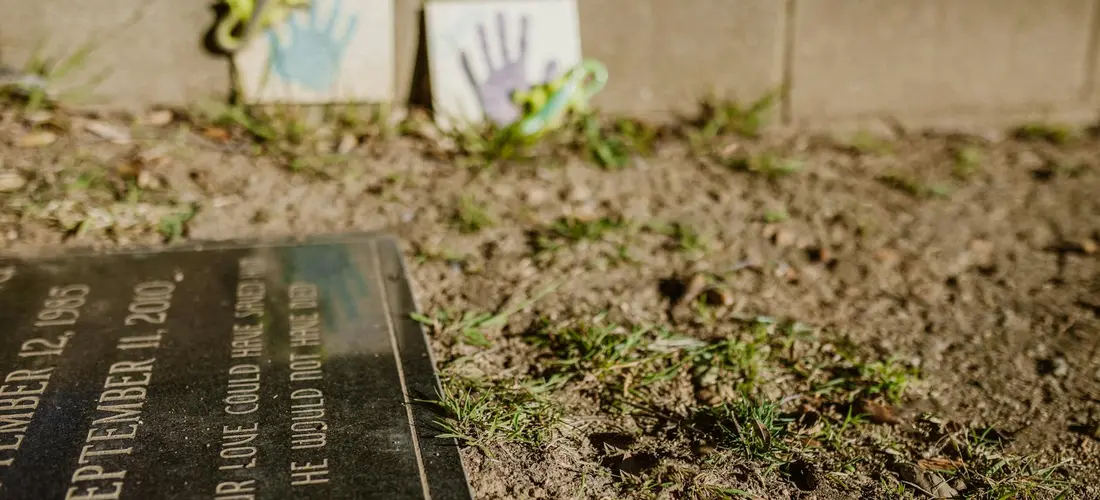 Close-up of a burial plot marker on dirt with blurred papers or cards in the background.