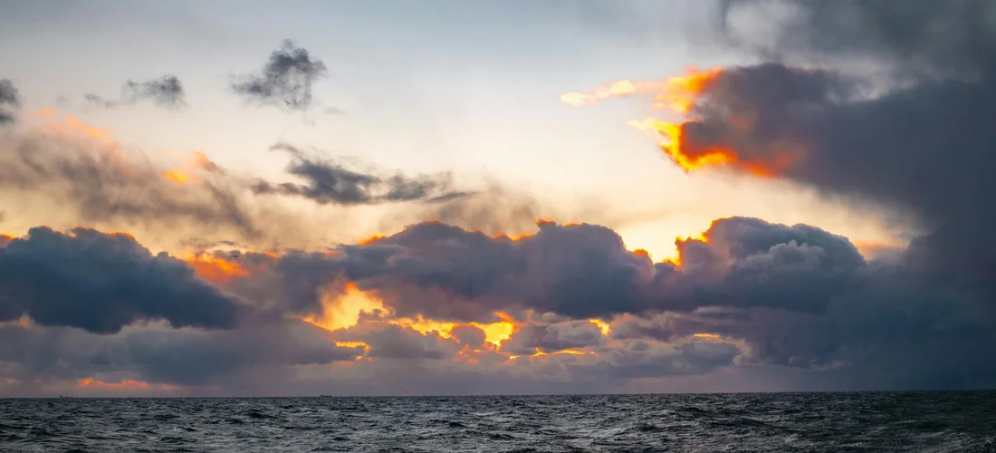 Sunset over the ocean with dark clouds and a glowing horizon
