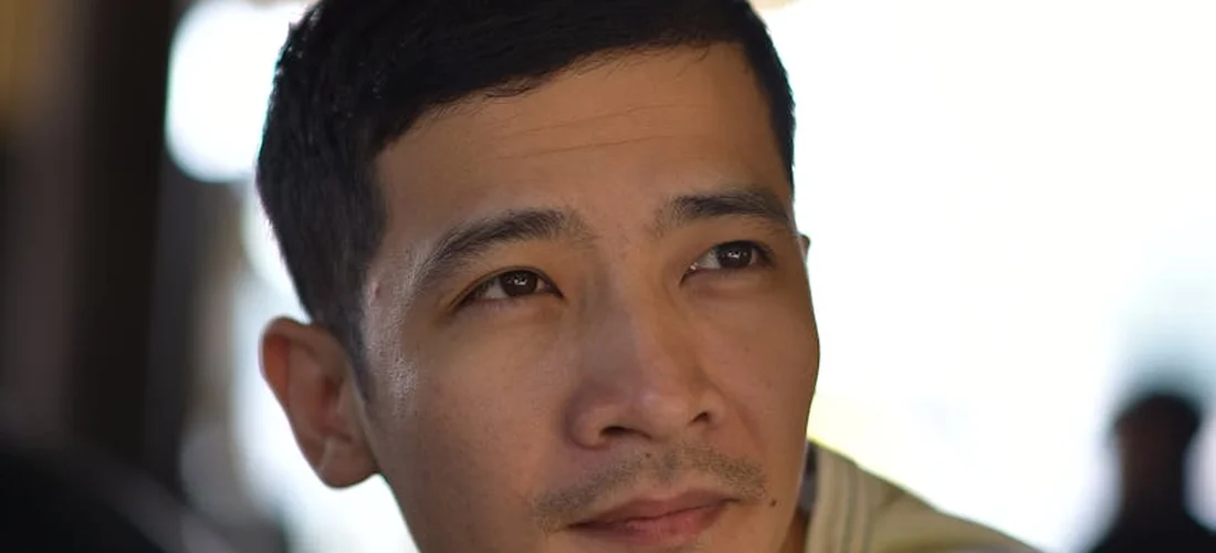 Close-up portrait of a man with short black hair looking off to the side, wearing a light casual shirt.