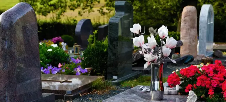 Gravestones in a cemetery with white and red flowers arranged at several grave sites.