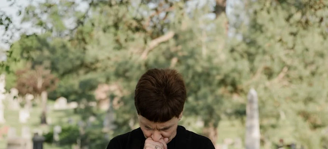 A person with bowed head in a cemetery, conveying solemn reflection tied to funeral rituals.