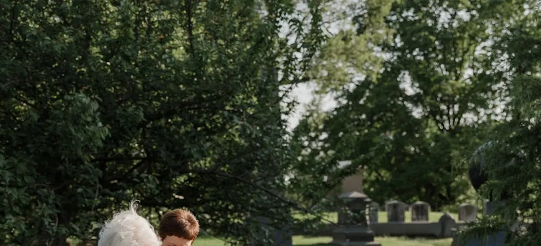 Two people at a cemetery with headstones and trees, reflecting on burial planning and costs.