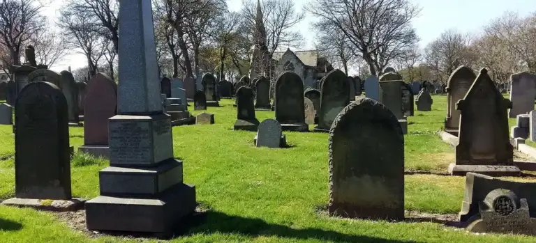 Graveyard with tombstones and monuments on a grassy field beneath leafless trees.