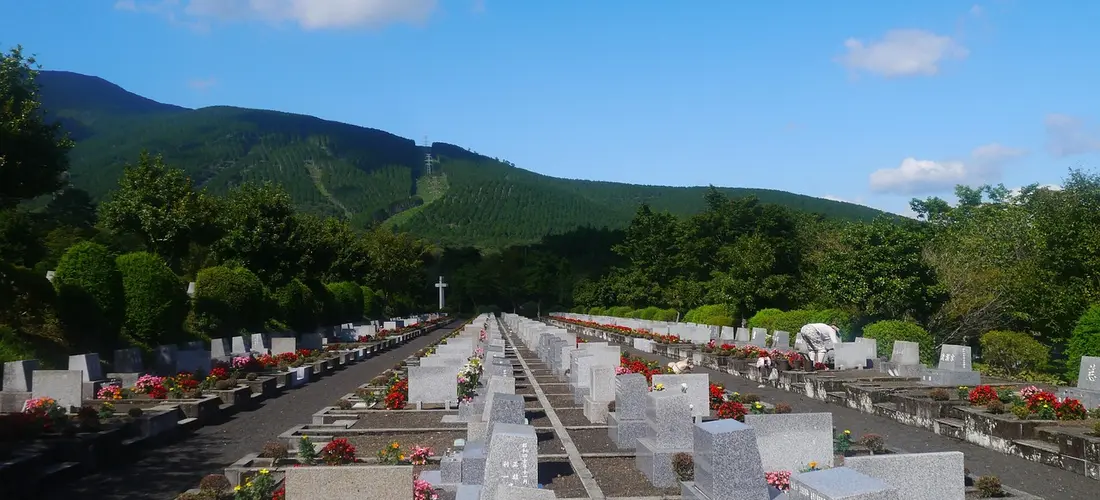 Rows of white gravestones in a large cemetery with green hills and a clear blue sky in the background.