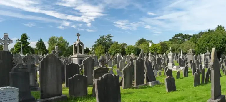 A cemetery filled with numerous weathered tombstones under a bright blue sky.