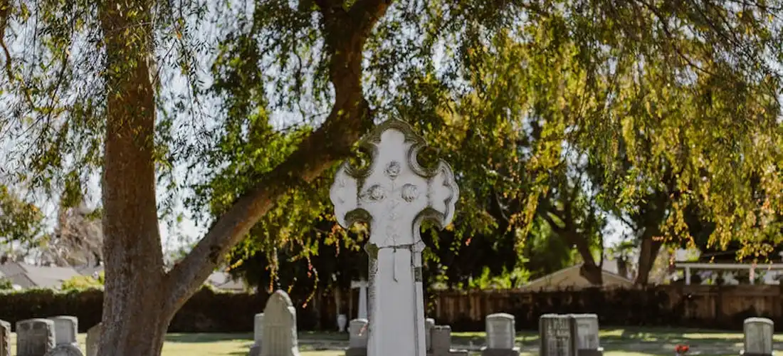A serene cemetery scene with trees, grass, and white grave markers, illustrating natural and eco-friendly burial options.