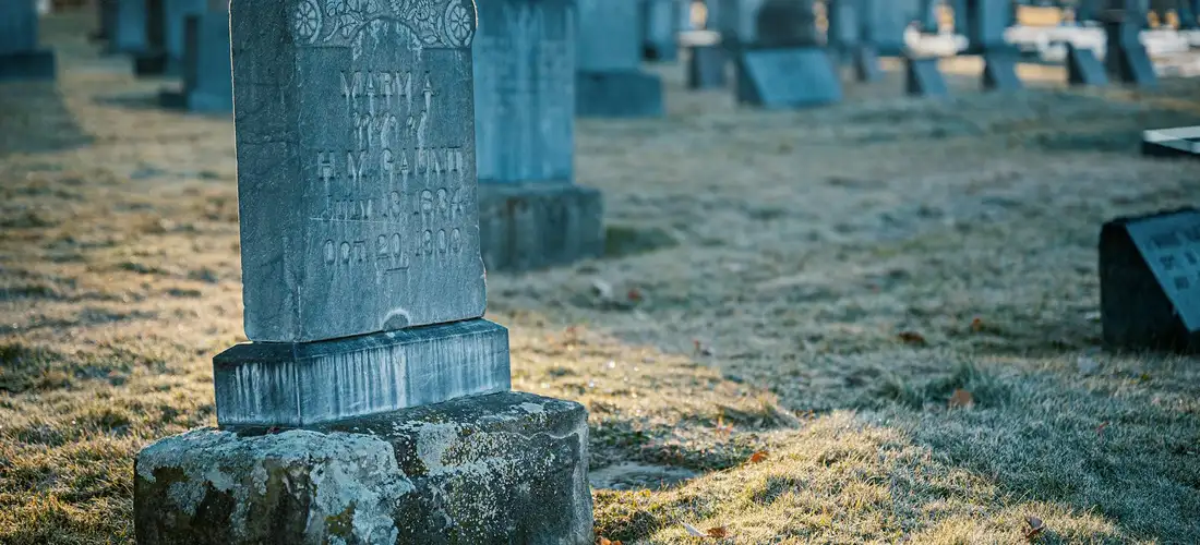 Close-up of a weathered gravestone in a cemetery with more headstones blurred in the background