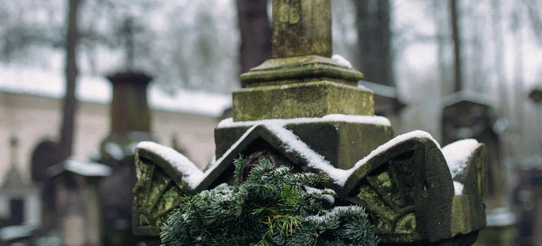 Close-up of a snow-dusted cemetery memorial with a wreath and evergreen foliage