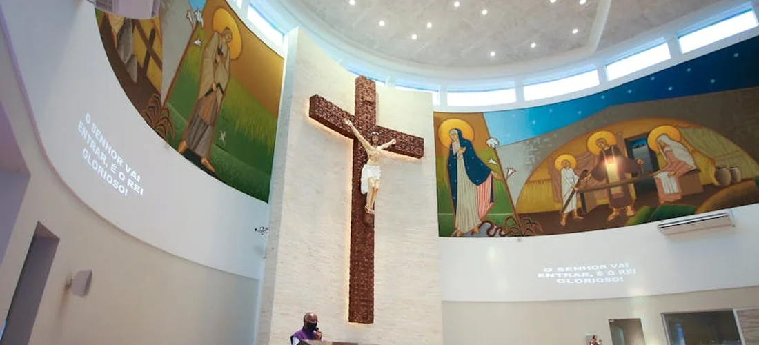 Interior of a church featuring a prominent crucifix at the center and colorful murals along the curved walls.