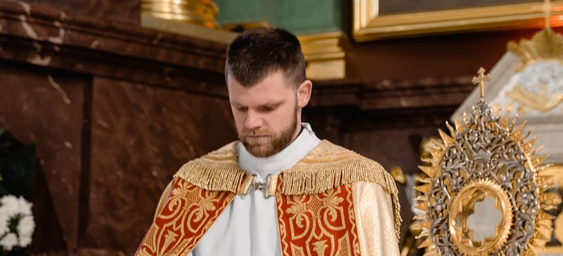 Priest in ornate red and gold vestments standing in a church interior.