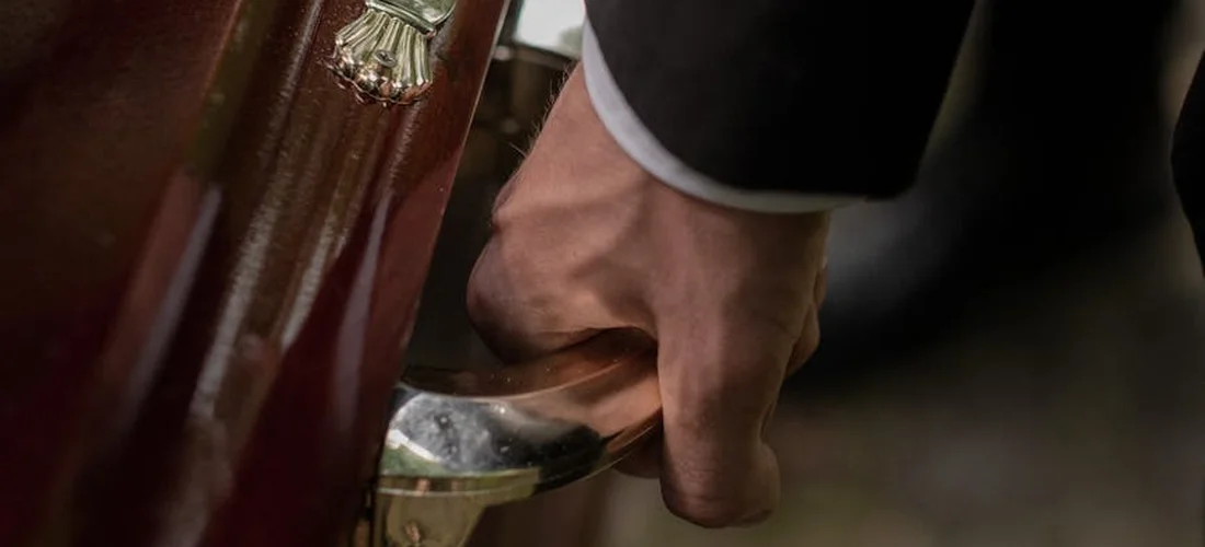 Close-up of a hand gripping the metal handle of a wooden casket