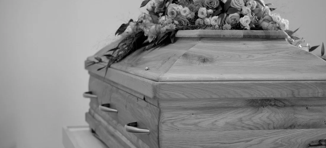 Black-and-white photo of a closed wooden coffin topped with a bouquet of flowers.