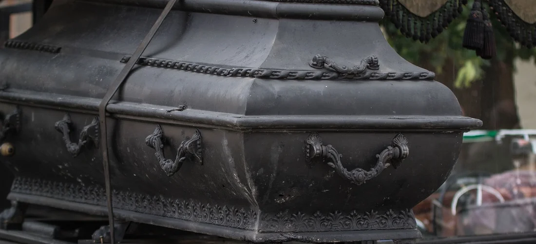 A dark ornately carved coffin with metal handles on display at a funeral home