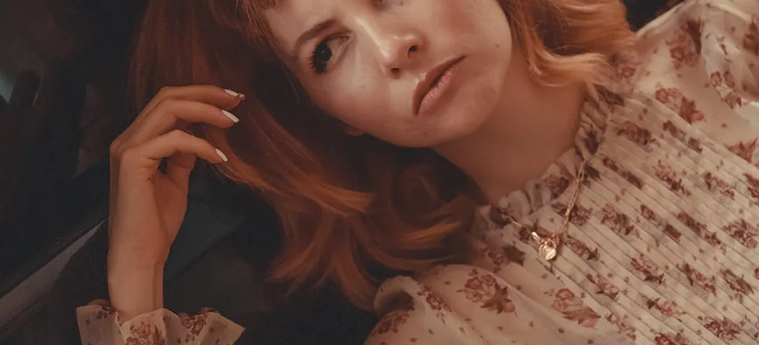 Portrait of a thoughtful woman with red hair lying down, wearing a floral blouse.