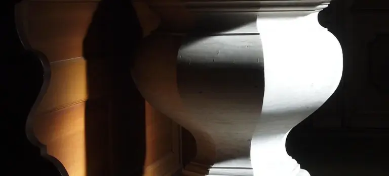 Close-up of a white marble pedestal with a curved, decorative edge against a dark background