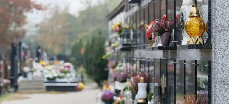Cremation niches on a cemetery wall with urns and flowers.
