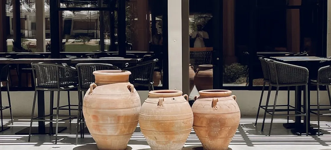 Three ceramic cremation urns displayed outdoors on a patio with tables and chairs in the background.