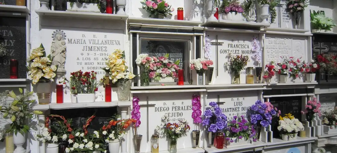 A row of white tombs and gravestones adorned with colorful flowers in a cemetery