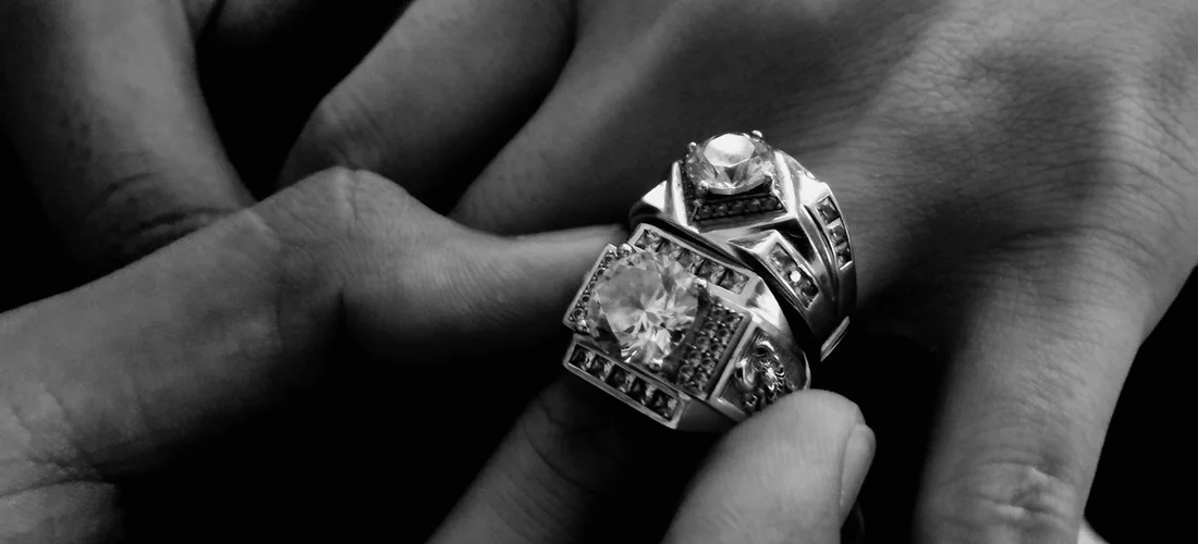 Close-up of hands holding ornate rings in a black-and-white photograph