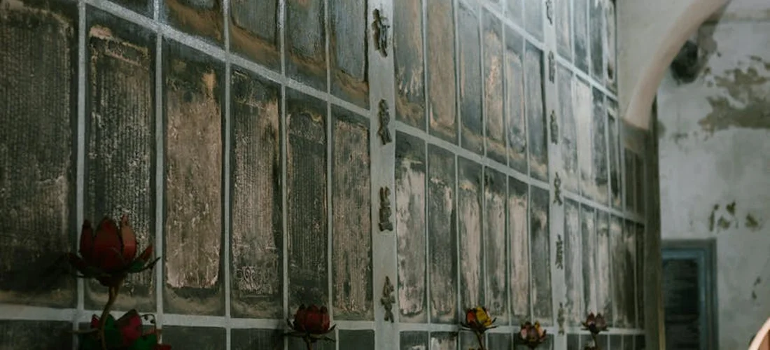 Dim mausoleum wall lined with memorial plaques, with red roses placed at the base.