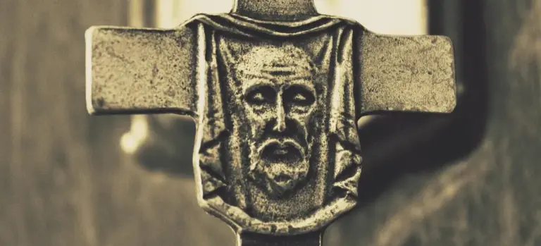 Close-up of a weathered stone crucifix with a carved face, symbolizing Christian rites surrounding death and burial.