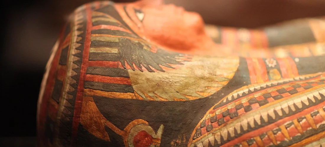 Close-up of a painted Egyptian coffin lid featuring geometric patterns and a sun disk motif, reflecting funerary ritual.