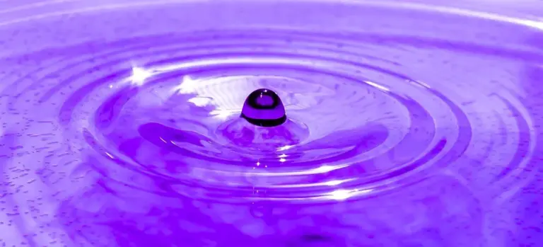 Close-up of a droplet causing ripples in a purple liquid.