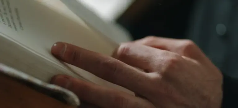 Close-up of hands holding and turning pages of an open book during a somber ceremony.