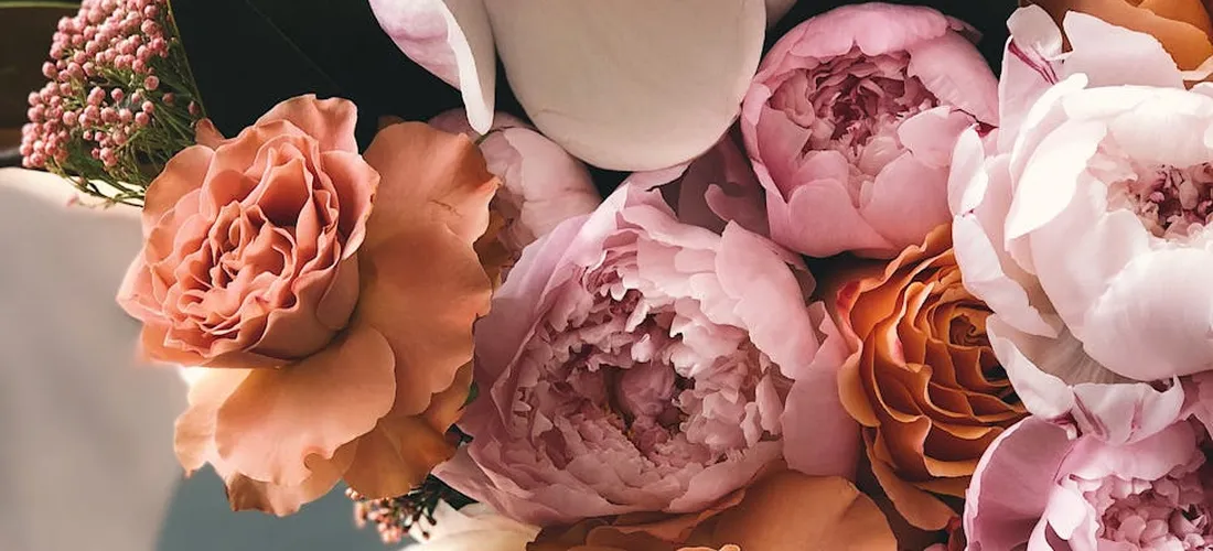 Close-up of a bouquet featuring pink and peach peonies and roses.