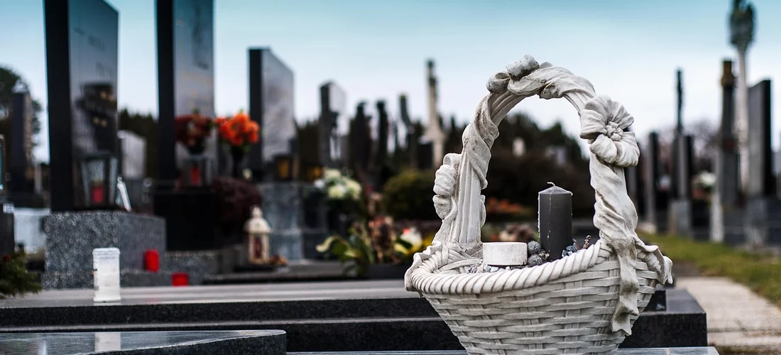 Cemetery scene with gravestones and flowers, foregrounded by a white wicker basket.