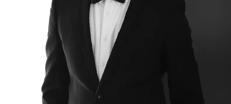 Close-up of a person wearing a black suit jacket, white dress shirt, and bow tie, representing traditional formal funeral attire.