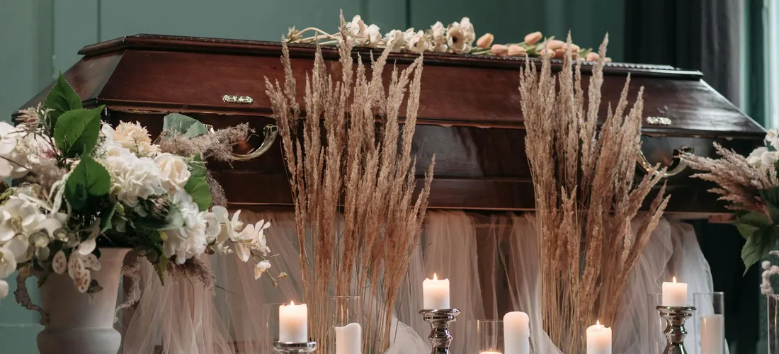 Funeral scene with a closed casket, candles, and tall floral arrangements
