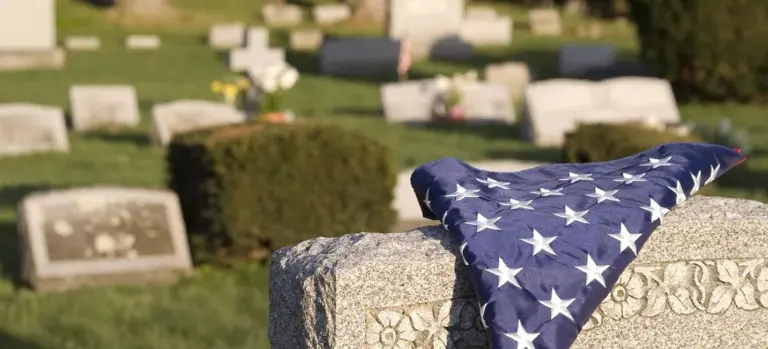 Folded American flag draped over a gravestone in a cemetery.