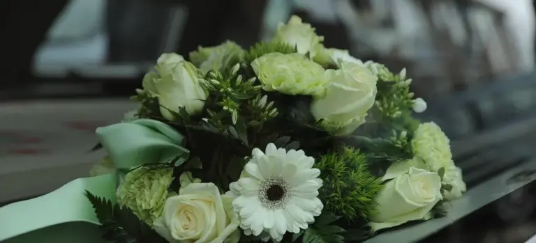 Bouquet of white roses and a white gerbera daisy with green filler flowers and a pale green ribbon, placed on a car hood.