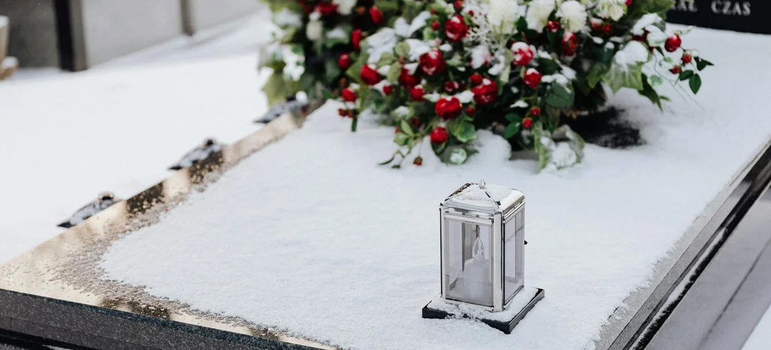 Gravestone covered in light snow with a lantern and a bouquet of red and white flowers