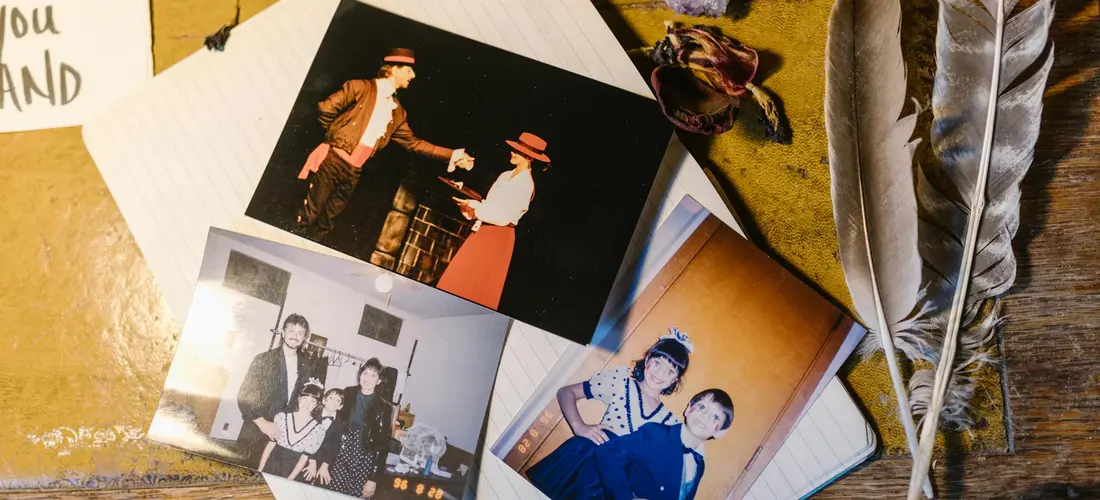 A collection of vintage photographs scattered on a wooden surface with a feather, suggesting memory and memorial keepsakes.