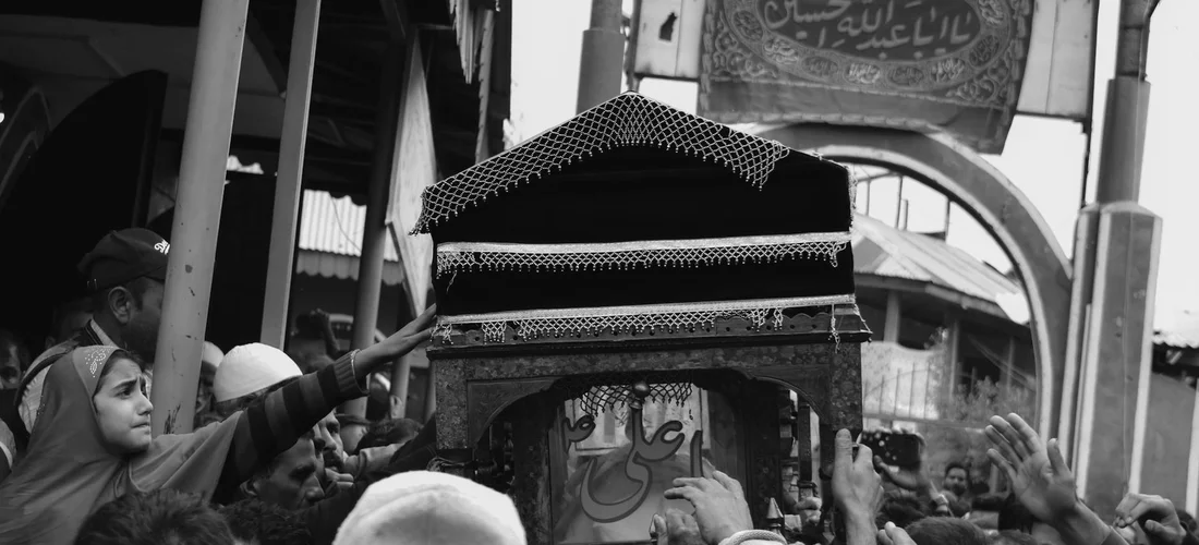 Crowd of mourners carries a coffin through a crowded street during a funeral procession.
