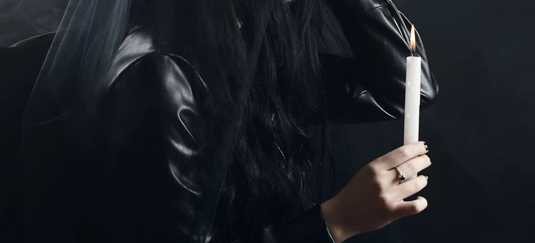 Person in dark clothing holding a lit candle in a dim setting