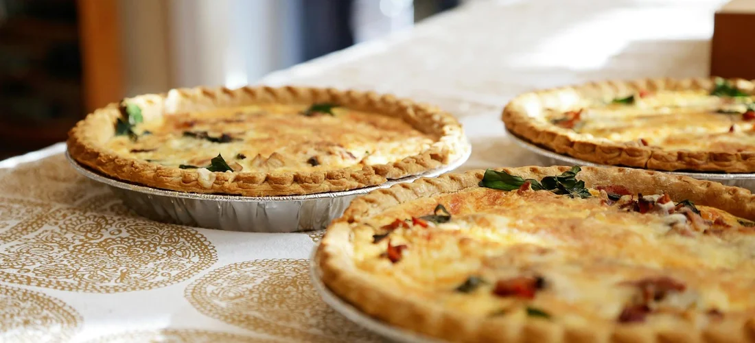 Three savory quiches on a light patterned tablecloth, ready to serve.