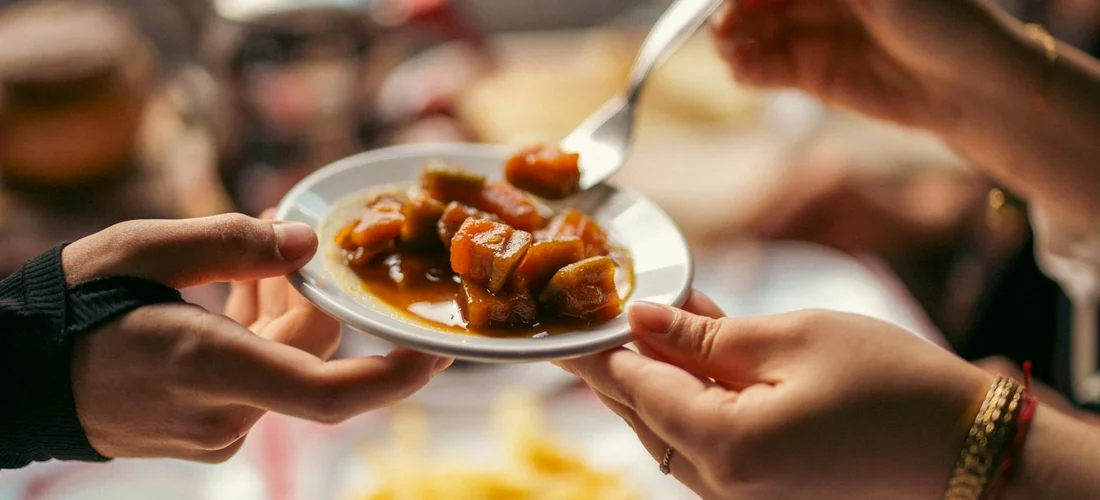 Hands pass a plate of hearty stew to guests at a casual funeral reception.